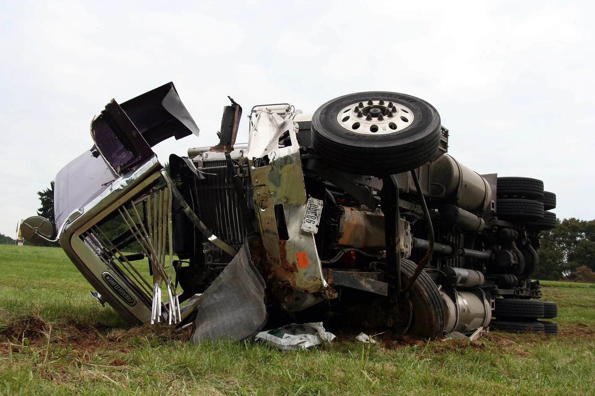 A heavily damaged semi-truck overturned on its side after an accident in a grassy area.