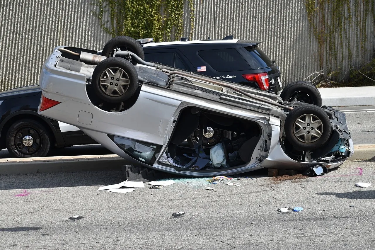 Overturned silver car after an accident on the road with police vehicle nearby