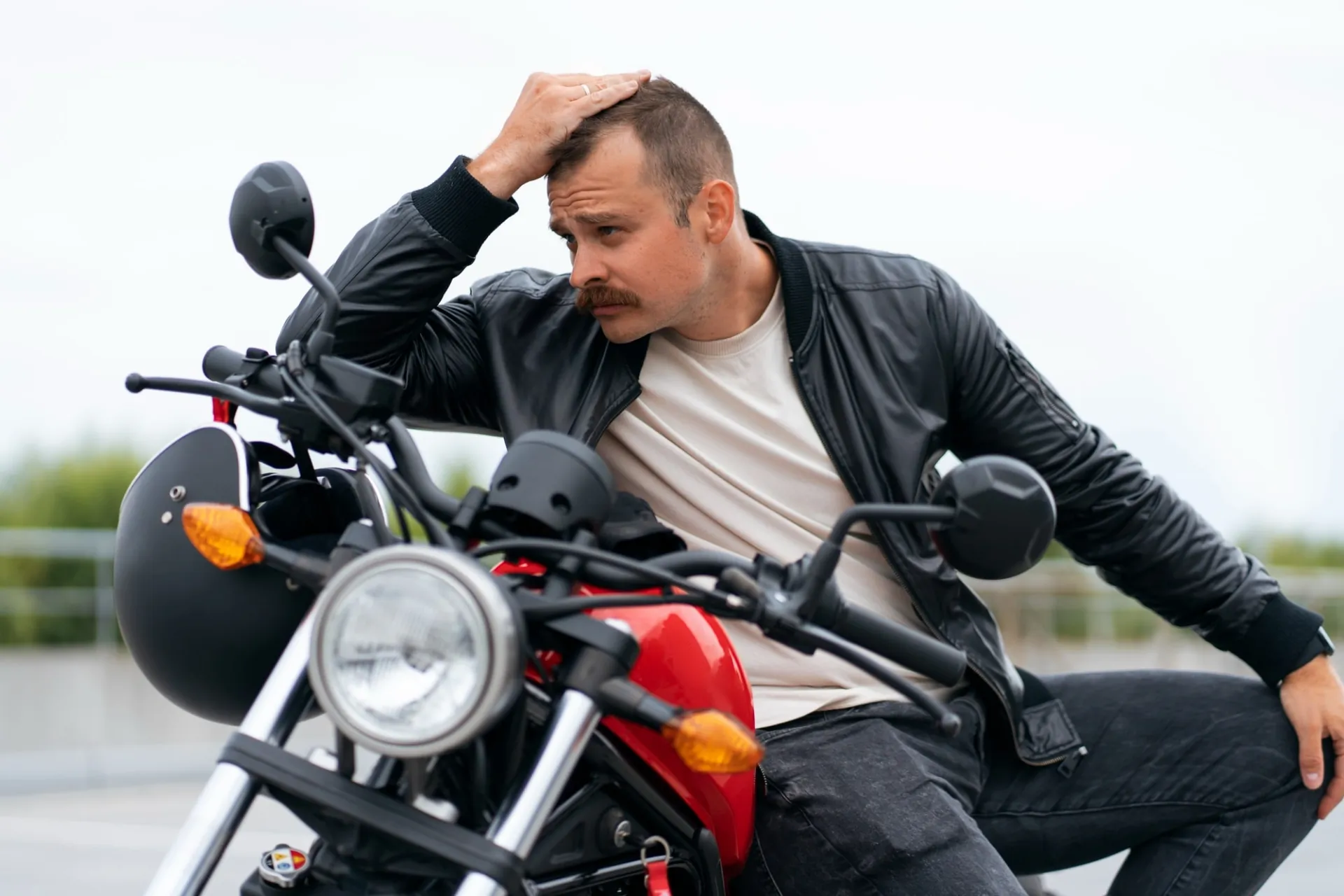 A concerned man sitting on his motorcycle, holding his head in distress, following a motorcycle accident.