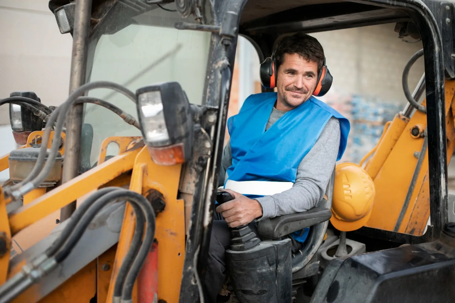 Male lift truck operator in safety gear sitting in a forklift, smiling
