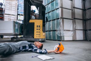 Worker lying on warehouse floor after a forklift accident, helmet and clipboard nearby