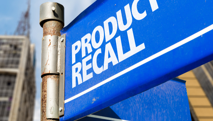 Blue sign with white text reading "PRODUCT RECALL" attached to a metal pole, with blurred buildings in the background.
