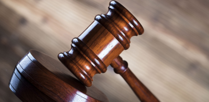 A wooden judge’s gavel rests on a sound block, symbolizing law and justice, with a blurred wooden background.
