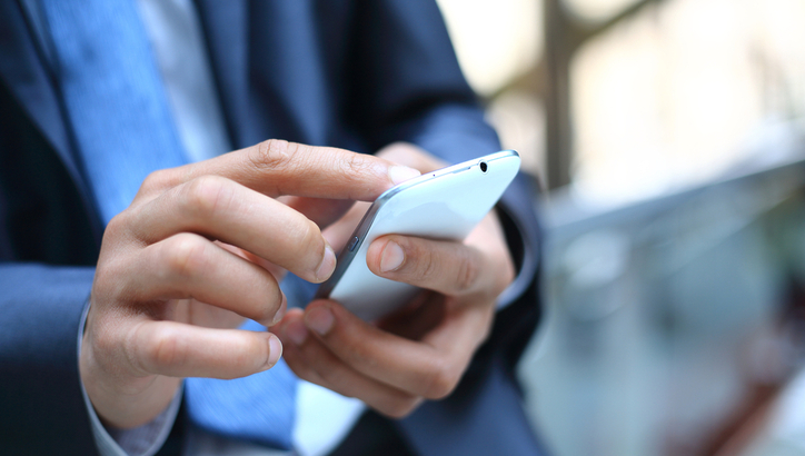 A person in a suit uses a smartphone, tapping on the screen with their right hand.