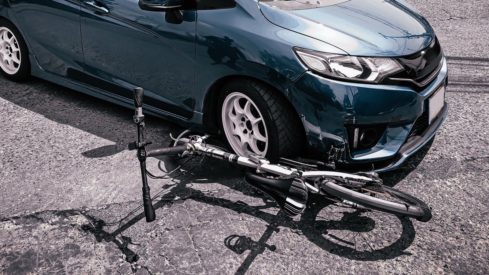 A blue car is parked on a road with a damaged bicycle lying on the ground next to its front bumper.