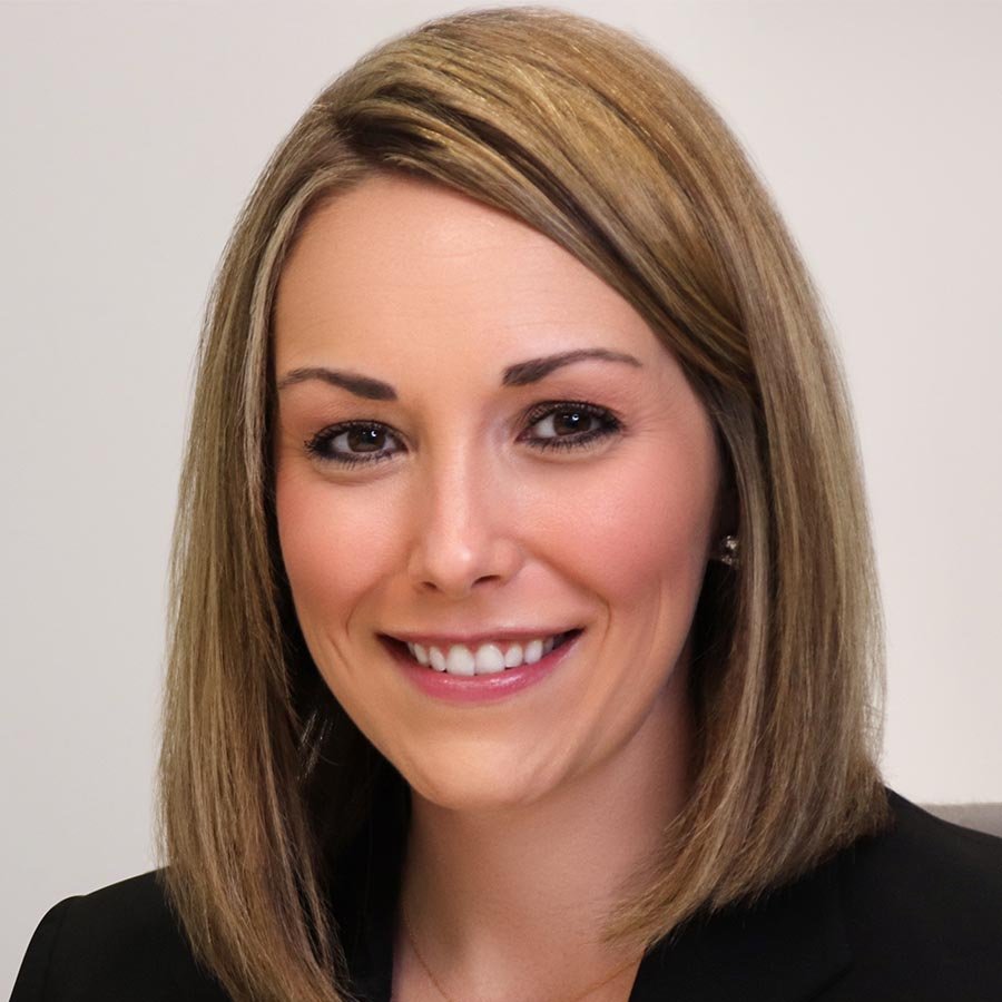 A woman with straight, shoulder-length blonde hair wearing a black blazer, smiling at the camera against a plain background.