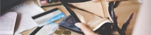 A person holds open an empty wallet on a table with credit cards, coins, and papers scattered nearby.