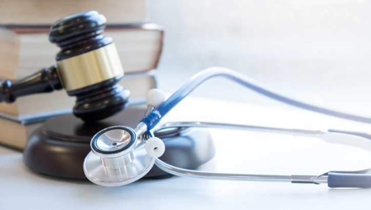 A judge’s gavel, a stethoscope, and stacked books are arranged on a desk, representing the intersection of law and medicine.