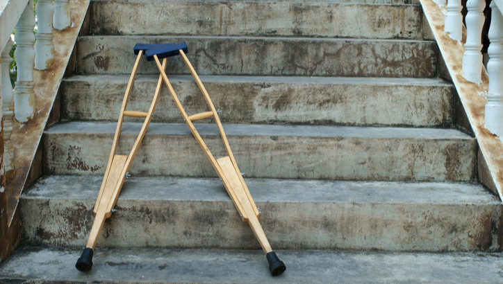 A pair of wooden crutches rests at the bottom of a worn concrete staircase with white railings on both sides.