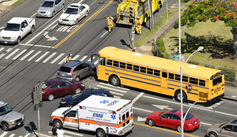 A school bus and a car are involved in a traffic accident at an intersection. Emergency vehicles and personnel are present at the scene.