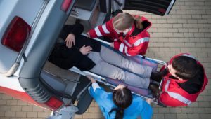 Three emergency responders load a person on a stretcher into an ambulance from an overhead perspective.