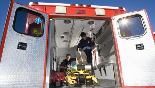 Two paramedics inside an open ambulance prepare a stretcher, with medical equipment visible around them.