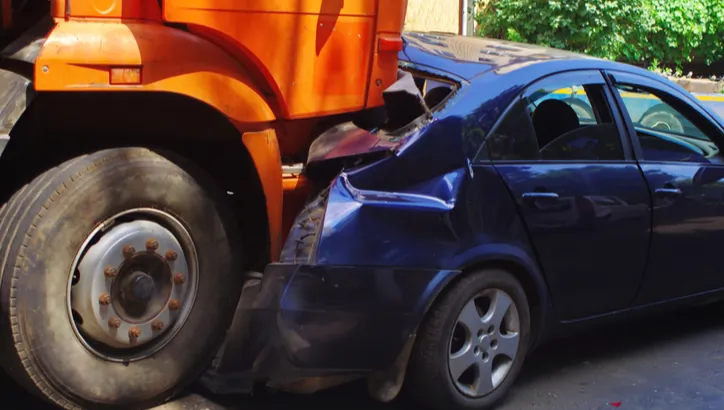 A blue car has crashed into the rear of an orange truck, resulting in visible damage to the carÔÇÖs front and the truckÔÇÖs rear.