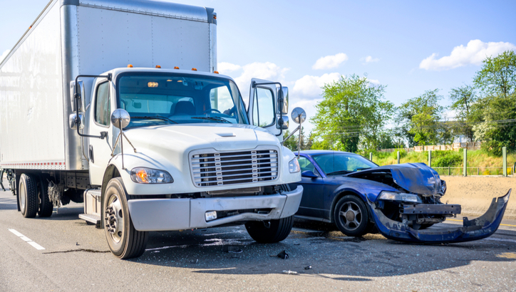 A large white truck and a black car involved in a collision on a road, with visible damage to the front of the car and minor damage to the truck.