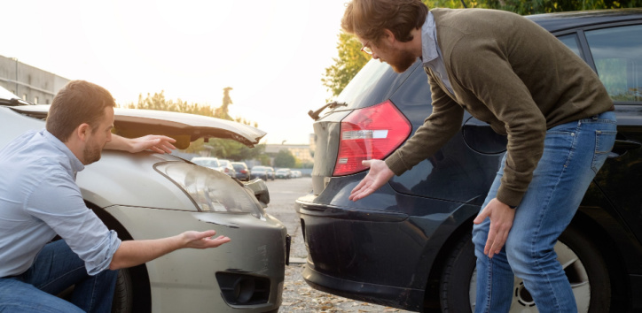Two men stand next to two cars involved in a rear-end collision, examining and gesturing at the damage on the vehicles.