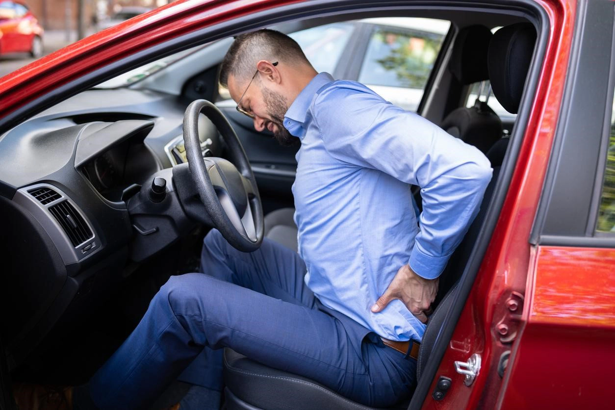 Man experiencing severe back pain while seated in his car after a collision, highlighting the impact of car accidents on spinal health.