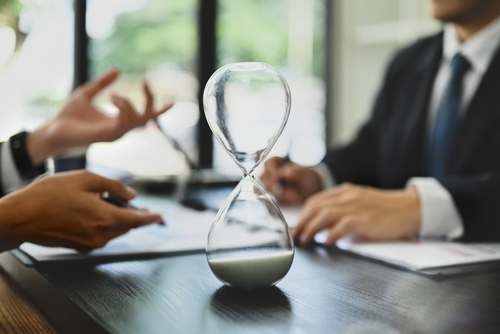 Hourglass on meeting table beside eyeglasses and blurred people in office