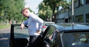 man exiting car while clutching lower back in visible pain