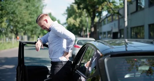 man exiting car while clutching lower back in visible pain