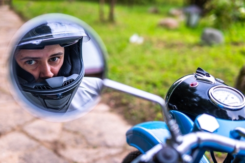 motorcyclist wearing helmet reflected in motorcycle side mirror outdoors