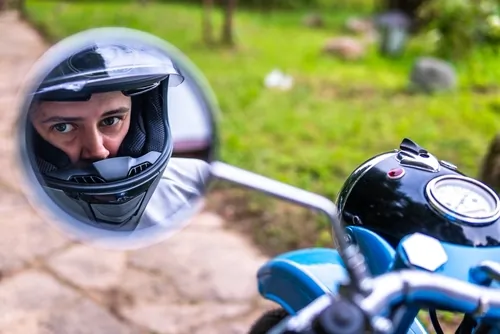 motorcyclist wearing helmet reflected in motorcycle side mirror outdoors