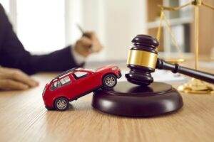 toy automobile crashed against judge gavel with scales of justice on desk