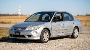 Honda Civic sedan with severe side door collision damage parked on rural roadside